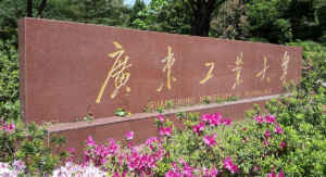 Marble Guangdong University of Technology Sign with Chinese characters amidst green shrubs and purple flowers