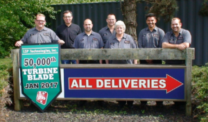 LSPT laser peening production team holding production milestone banner next to delivery sign