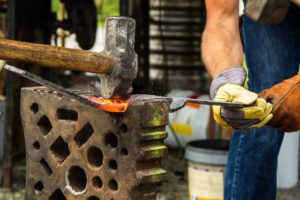 blacksmith hammering hot glowing metal piece wearing heavy gloves