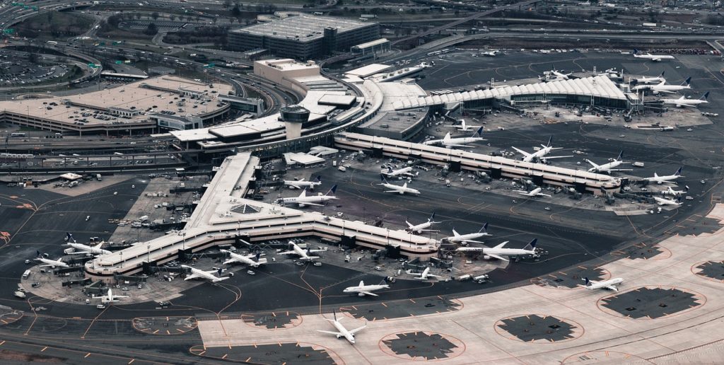 Large airport seen from above with white airplanes surrounding long terminals