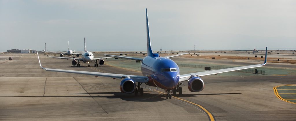 A line of passenger jets taxi down a taxiway as seen from the front