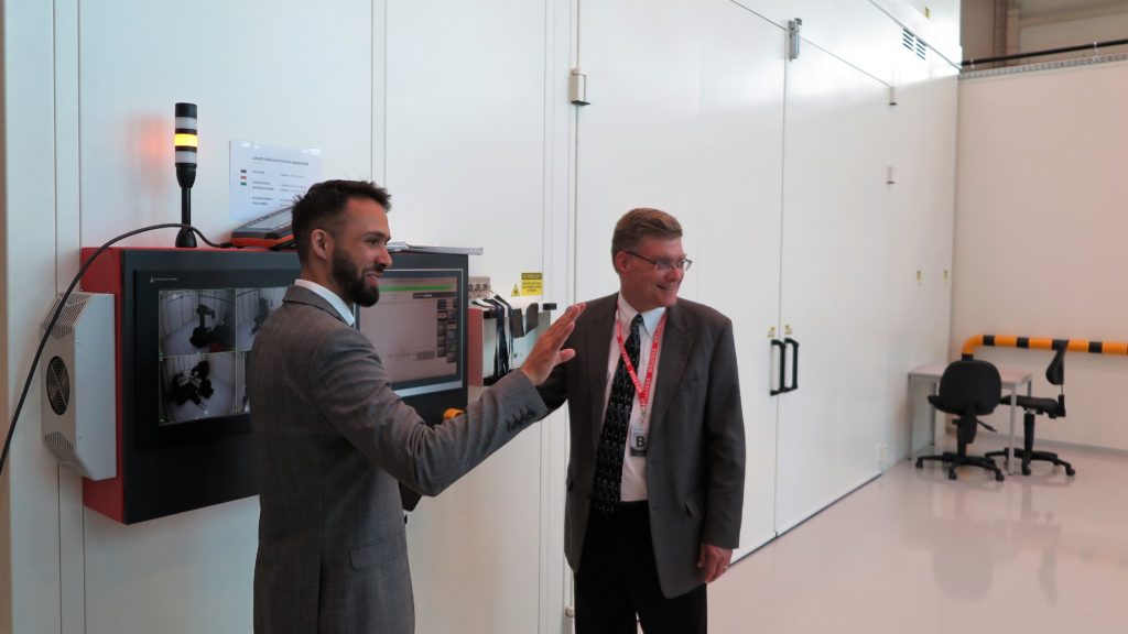 two men standing at a control panel for a laser peening system